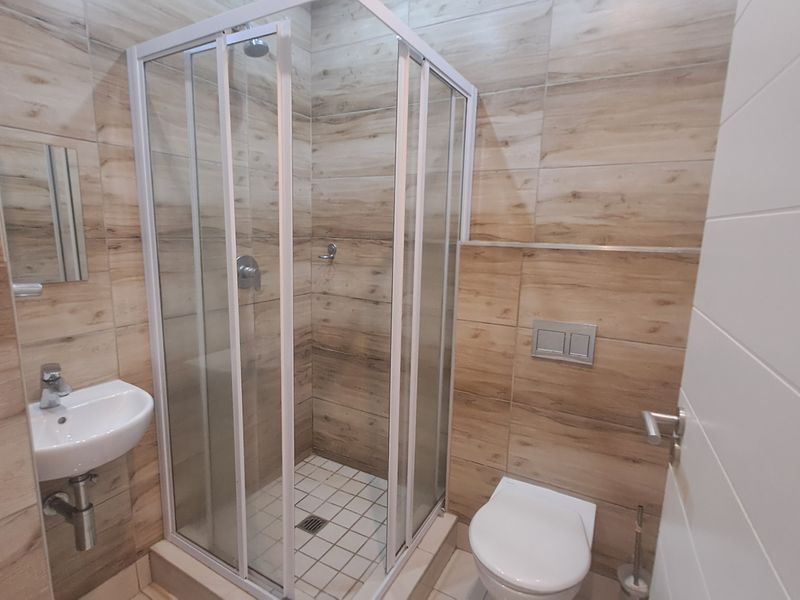 Modern bathroom featuring a glass shower enclosure, wall-mounted basin, and wall-hung toilet with wood-look tiled walls.