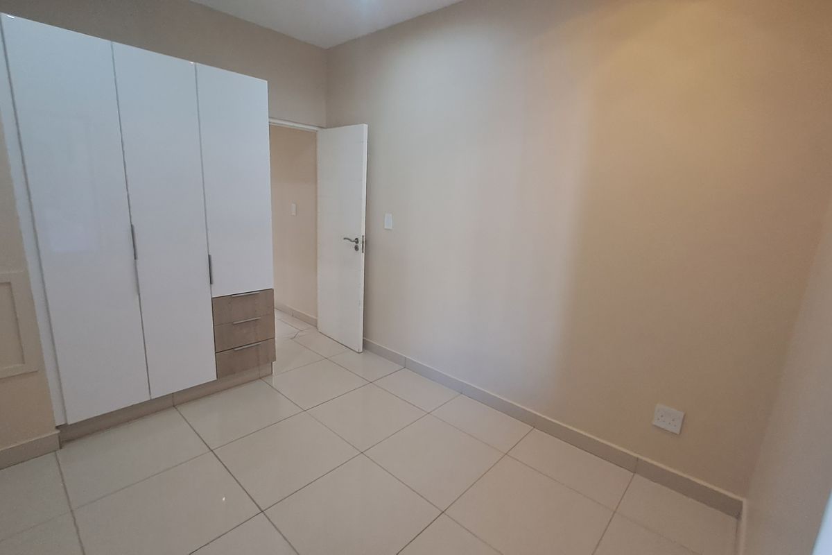 A clean, empty bedroom featuring neutral wall tones, modern tiled flooring, and a built-in wardrobe with integrated drawer storage.