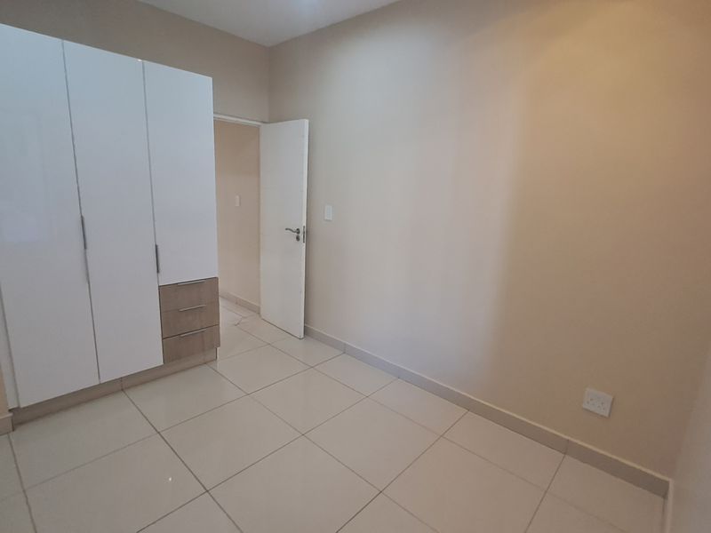 A clean, empty bedroom featuring neutral wall tones, modern tiled flooring, and a built-in wardrobe with integrated drawer storage.