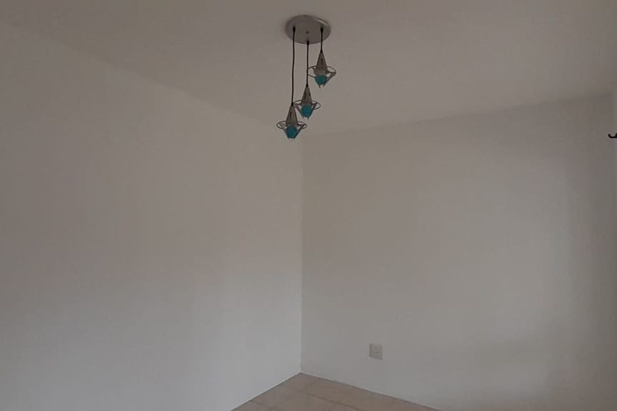 A bright, empty living room featuring tiled flooring, a modern pendant light fixture, and security bars on the window.