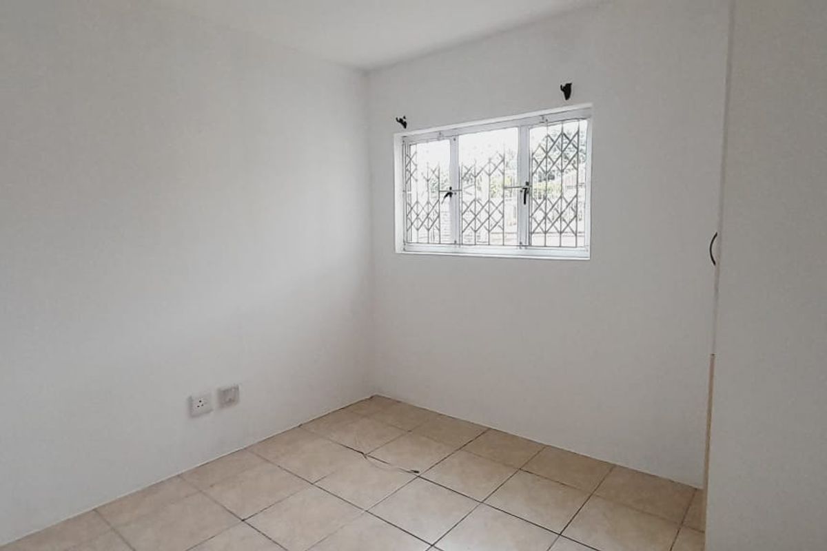 A vacant bedroom featuring neutral tiled flooring, white walls, and a window fitted with security bars.