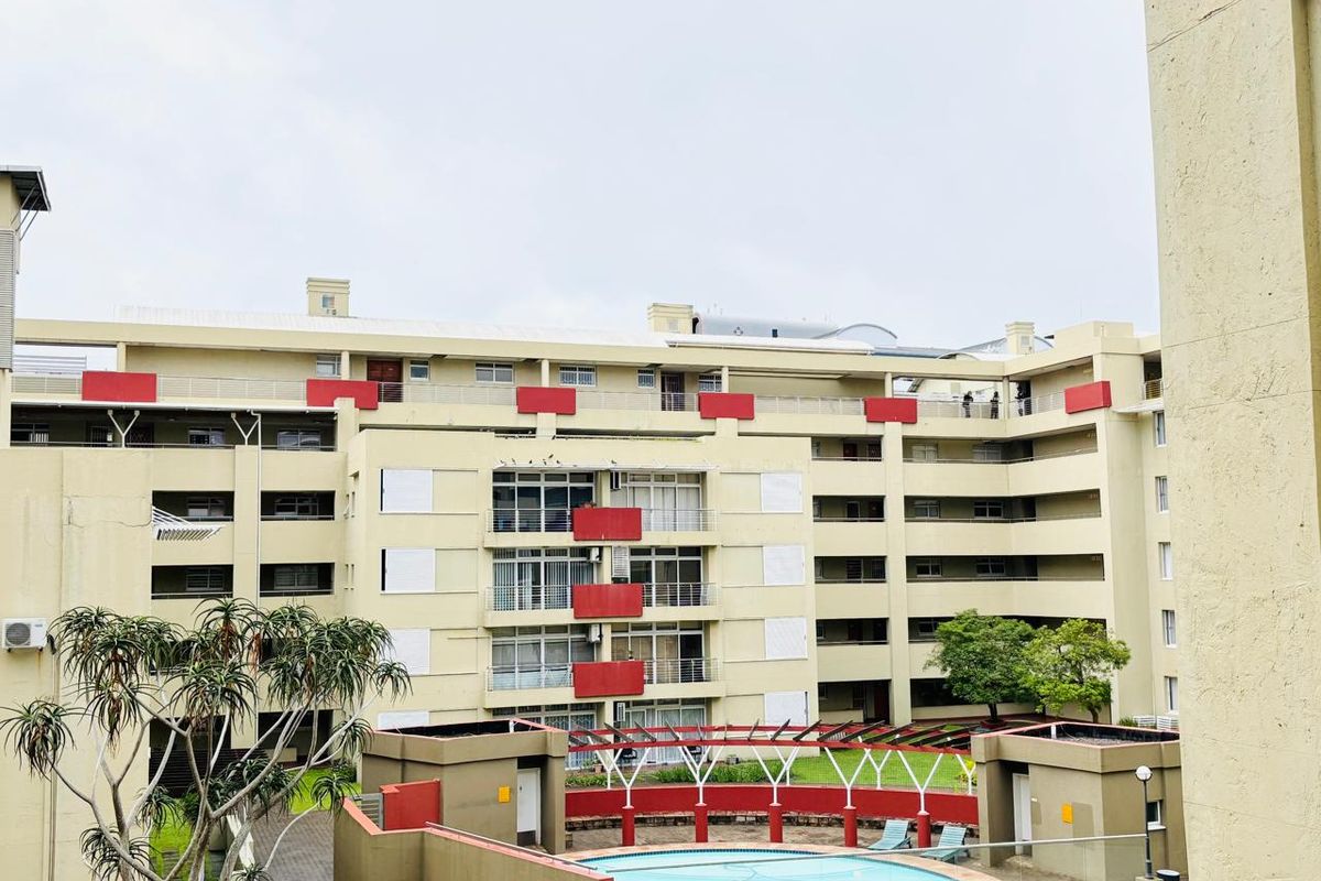 Exterior view of a multi-story apartment complex featuring a central swimming pool, landscaped garden areas, and private balconies with metal railings.