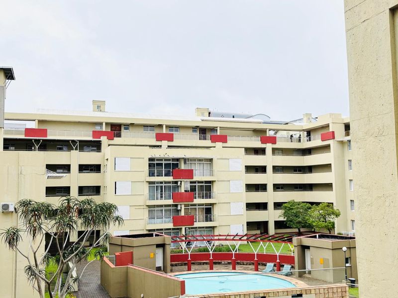 Exterior view of a multi-story apartment complex featuring a central swimming pool, landscaped garden areas, and private balconies with metal railings.