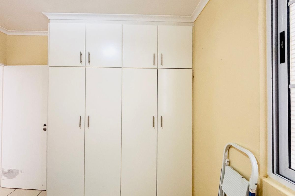 A bedroom featuring floor-to-ceiling built-in cupboards, tiled flooring, and a window with an aluminium frame.