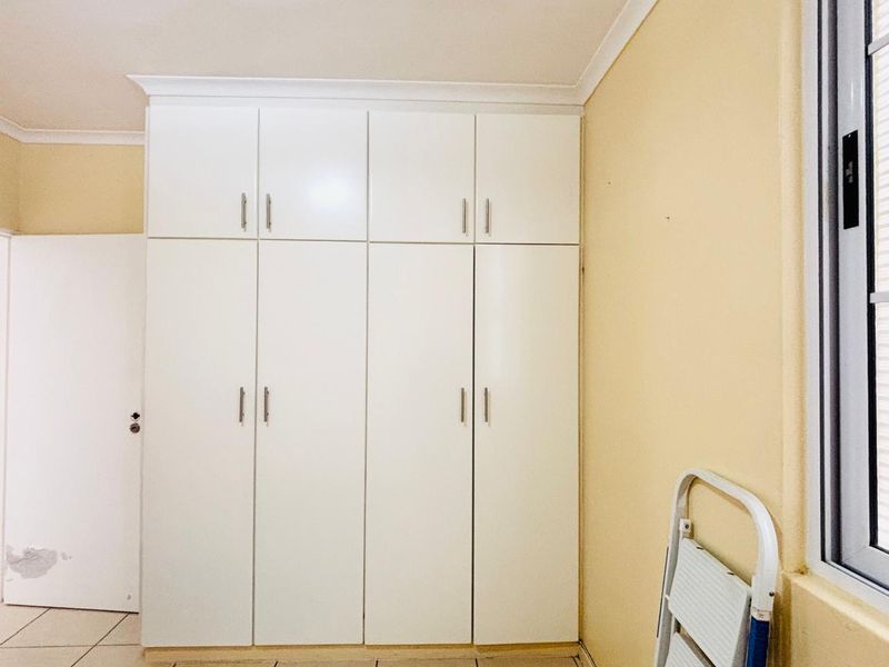 A bedroom featuring floor-to-ceiling built-in cupboards, tiled flooring, and a window with an aluminium frame.