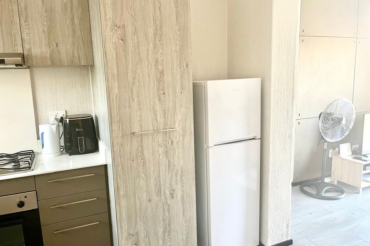 A compact kitchen area featuring light wood-grain cabinetry, a built-in oven, and a gas hob, seamlessly integrated into an open-plan living space.