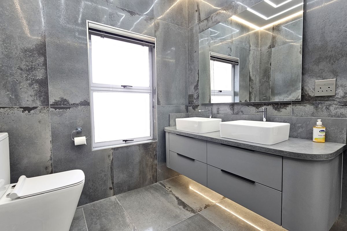 Modern bathroom featuring a floating double vanity with vessel sinks, large format metallic-look wall tiles, and integrated LED lighting.