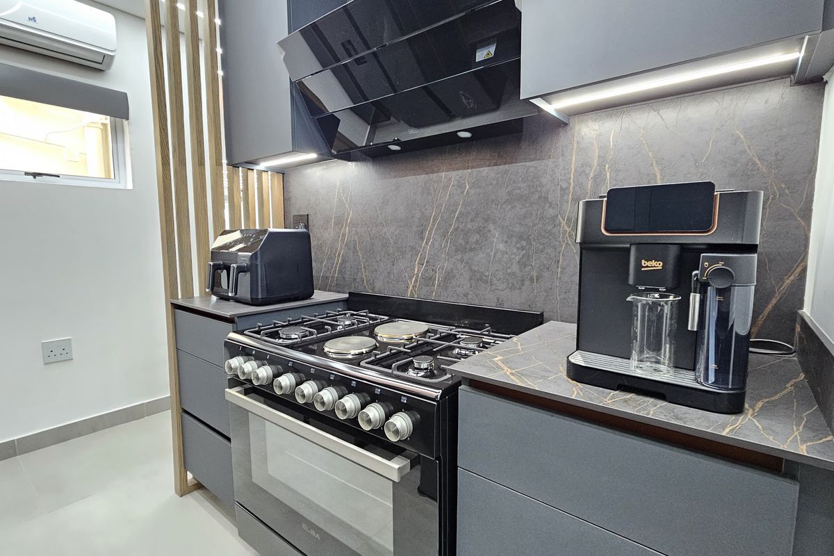 Modern kitchen featuring dark grey cabinetry, stone-look backsplash, integrated lighting, and a high-end gas stove with an extractor fan.