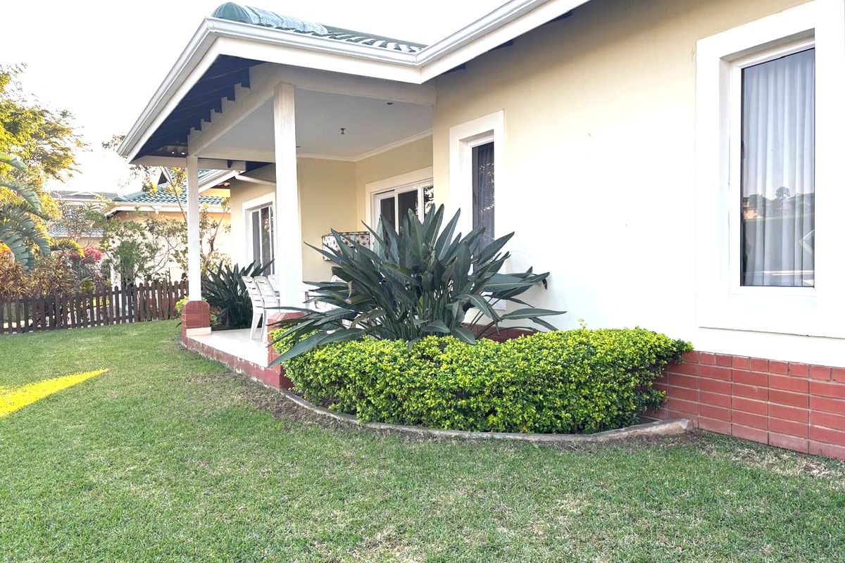 A well-maintained rear exterior view featuring a covered patio, brick foundation detailing, and established garden landscaping.