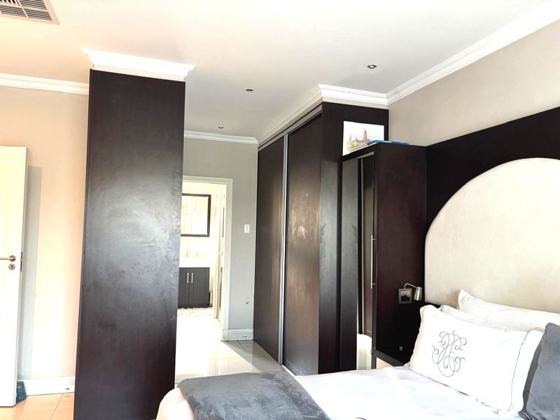 A well-maintained bedroom featuring dark wood built-in cupboards, recessed lighting, crown molding, and tiled flooring, with an adjoining bathroom visible.