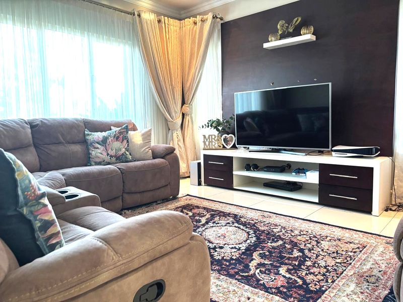 A comfortable living room featuring tiled flooring, a dark accent wall with a floating shelf, and large windows with floor-to-ceiling curtains.