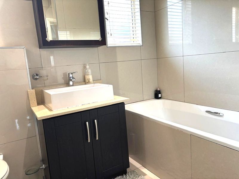 Modern bathroom featuring a vessel sink on a dark vanity cabinet, a built-in bathtub, and neutral wall tiling.