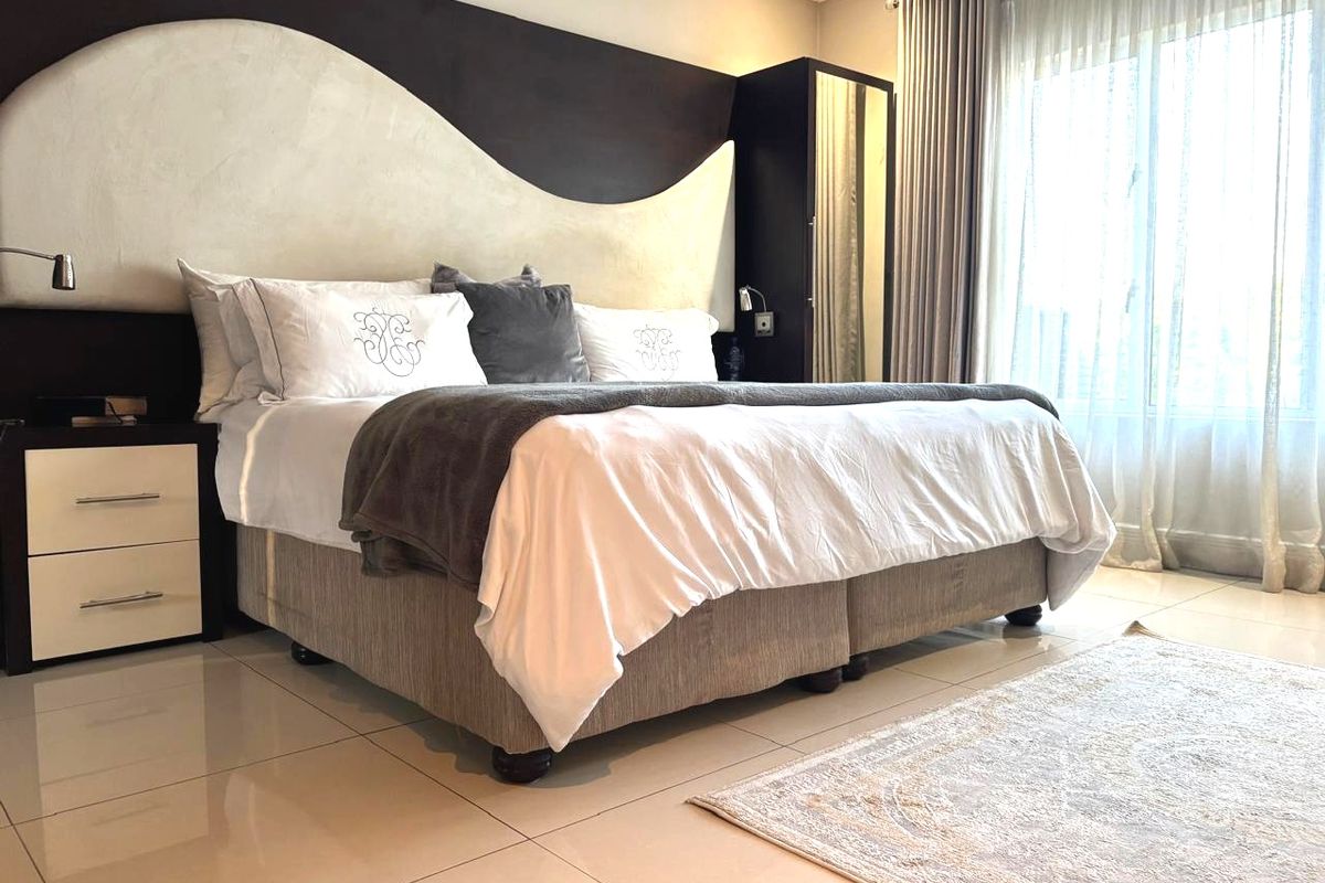 A well-maintained bedroom featuring a custom built-in headboard, tiled flooring, and integrated wardrobe storage with natural light from the window.