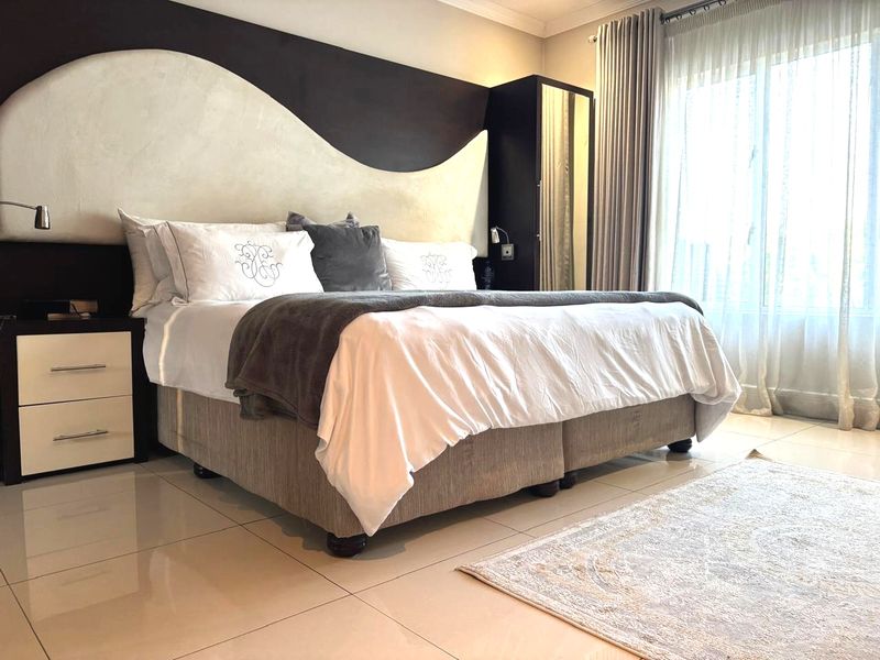 A well-maintained bedroom featuring a custom built-in headboard, tiled flooring, and integrated wardrobe storage with natural light from the window.