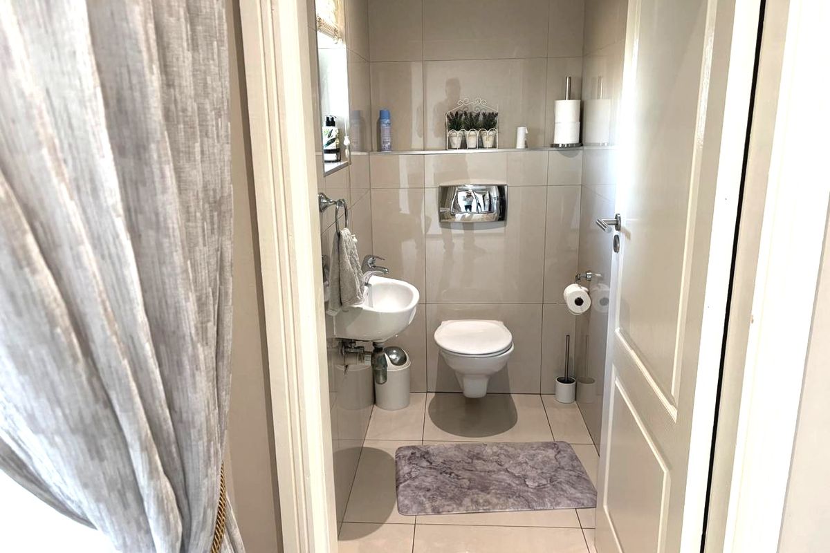 A compact, modern guest bathroom featuring neutral wall-to-wall tiling, a wall-mounted toilet with a concealed cistern, and a sleek wall-mounted basin.