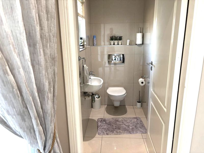 A compact, modern guest bathroom featuring neutral wall-to-wall tiling, a wall-mounted toilet with a concealed cistern, and a sleek wall-mounted basin.