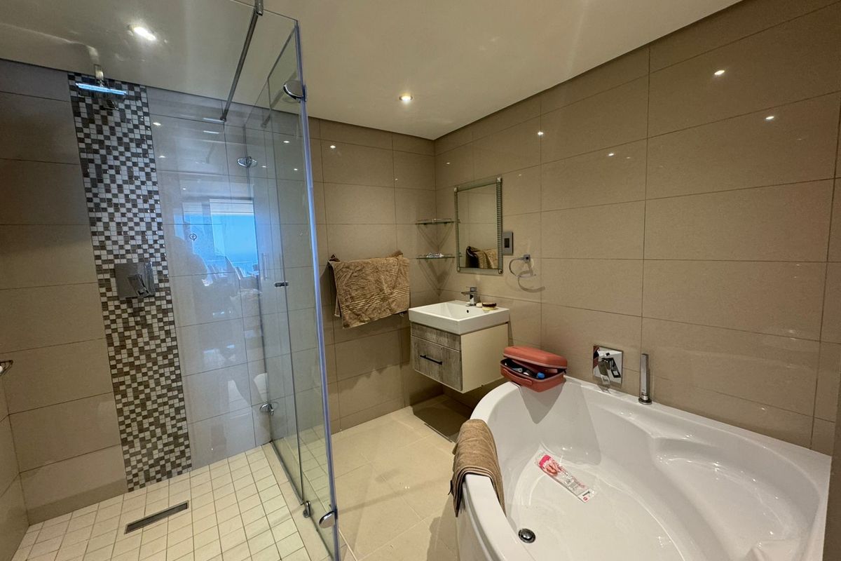 Modern bathroom featuring a glass-enclosed walk-in shower with mosaic tile accents, a wall-mounted vanity, and a corner soaking tub with chrome fixtures.
