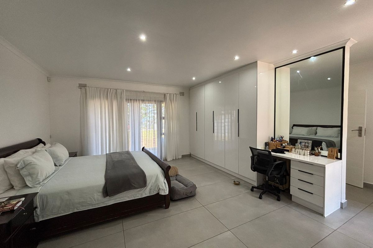 Spacious bedroom featuring large format floor tiles, recessed downlighting, extensive built-in cabinetry, and a dedicated vanity area with a large integrated mirror.