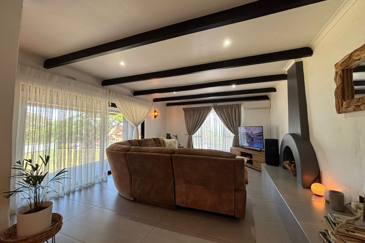 Spacious living room featuring exposed ceiling beams, large sliding glass doors providing natural light, and a modern built-in fireplace with a hearth.