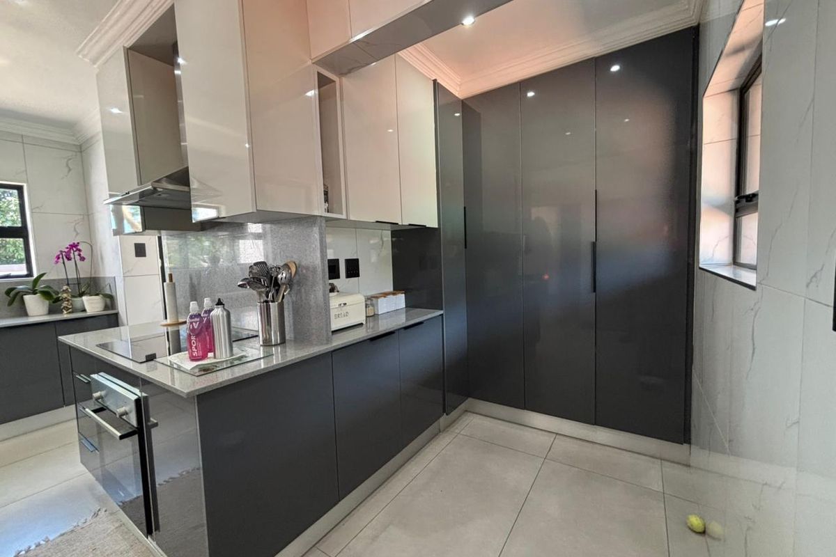 Modern kitchen featuring high-gloss cabinetry, stone countertops, integrated oven, and sleek tiled flooring with ample storage space.