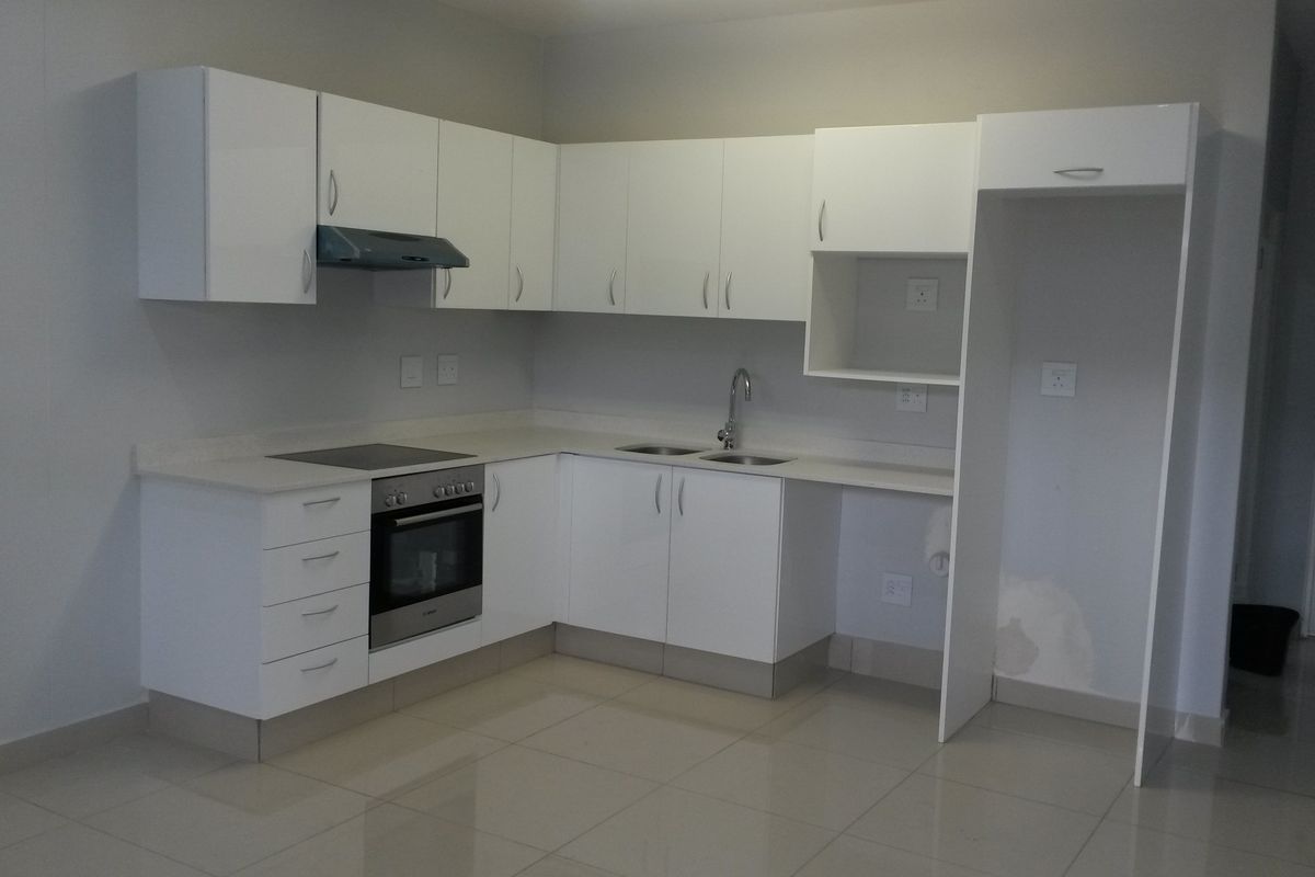 A clean, modern kitchen featuring white cabinetry, built-in oven, electric hob, and stone countertops, offering a functional and bright workspace.