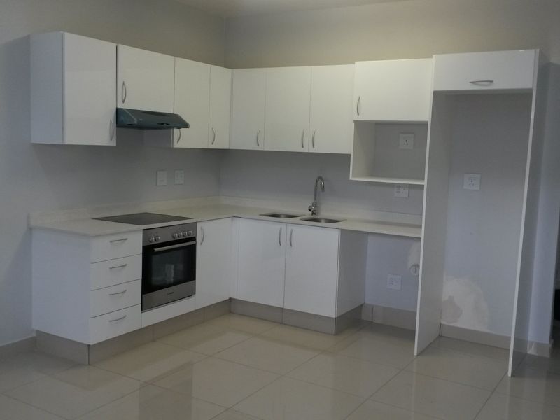 A clean, modern kitchen featuring white cabinetry, built-in oven, electric hob, and stone countertops, offering a functional and bright workspace.