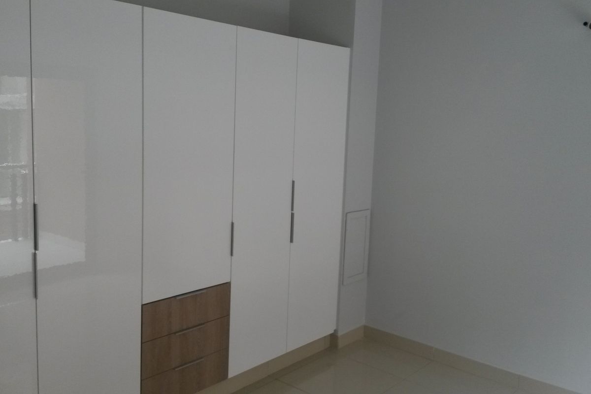 A clean, empty bedroom featuring modern white built-in wardrobes with integrated wood-tone drawers and neutral tiled flooring.