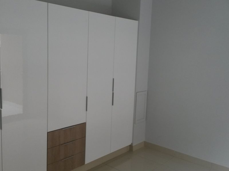 A clean, empty bedroom featuring modern white built-in wardrobes with integrated wood-tone drawers and neutral tiled flooring.