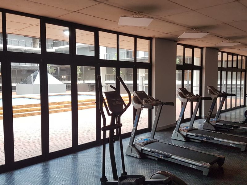 A well-lit apartment complex gym featuring rubber flooring and large glass doors overlooking the outdoor pool area.