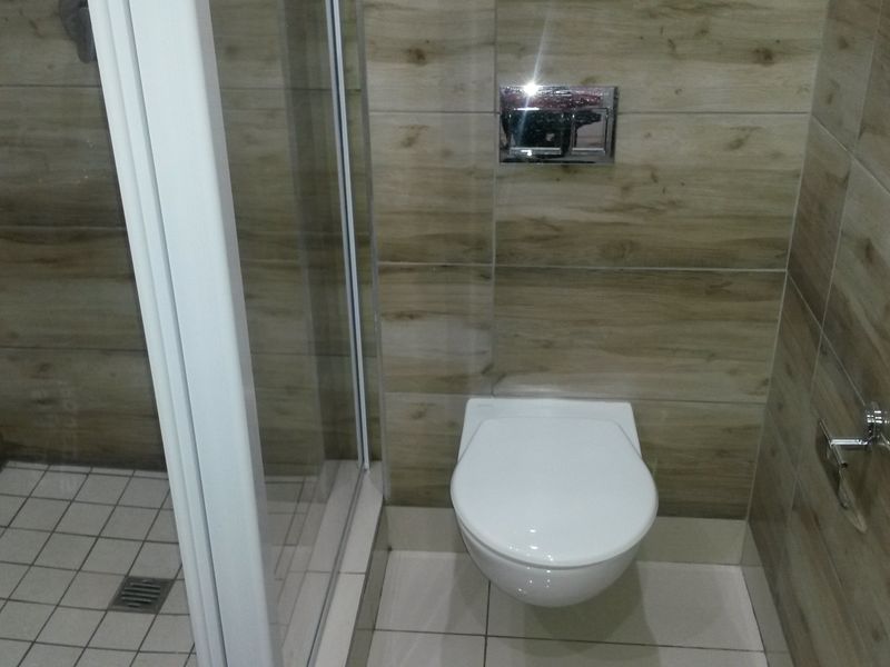 Modern bathroom featuring a wall-mounted toilet with a concealed cistern and a glass-enclosed shower, finished with contemporary wood-look wall tiling.