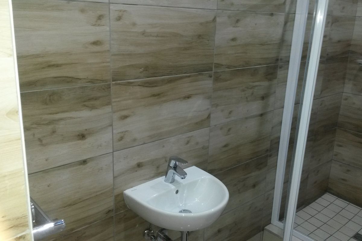 Modern bathroom featuring wood-look wall tiling, a wall-mounted basin with chrome mixer tap, and a walk-in shower with a glass screen.