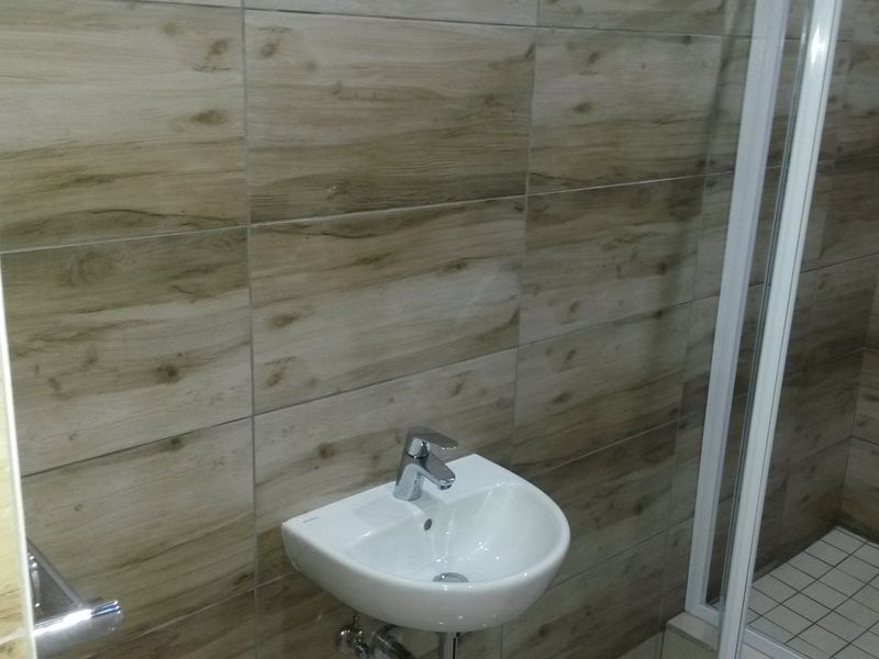 Modern bathroom featuring wood-look wall tiling, a wall-mounted basin with chrome mixer tap, and a walk-in shower with a glass screen.