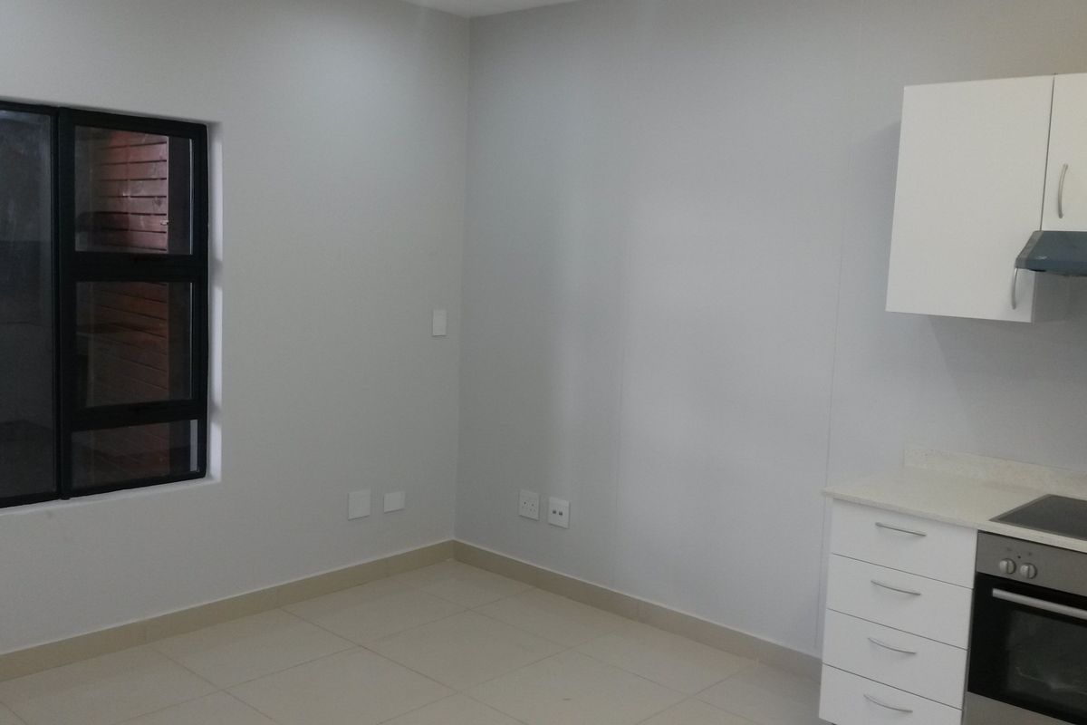 A clean, modern kitchen area featuring white built-in cabinetry, an integrated oven and hob, tiled flooring, and a large window.
