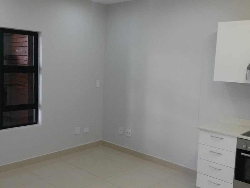 A clean, modern kitchen area featuring white built-in cabinetry, an integrated oven and hob, tiled flooring, and a large window.