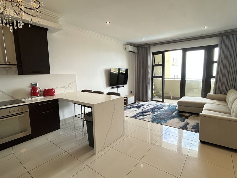 Modern open-plan living area featuring a sleek kitchen with stone countertops, built-in appliances, tiled flooring, and direct access to a private balcony.