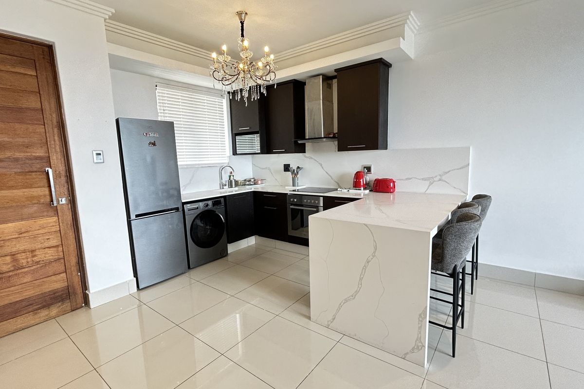 Modern kitchen featuring dark cabinetry, white quartz countertops with waterfall edge, breakfast bar, and integrated appliances, complemented by elegant crown molding and tiled floors.