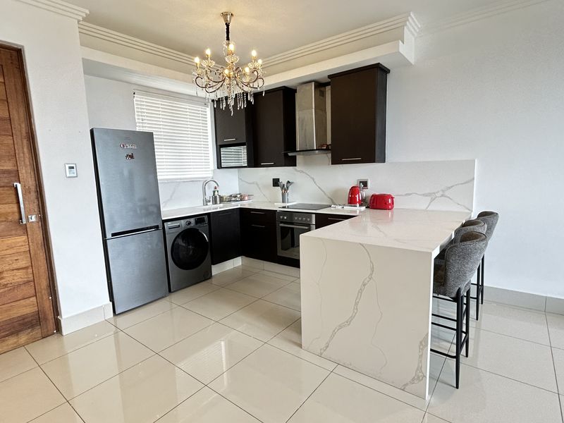 Modern kitchen featuring dark cabinetry, white quartz countertops with waterfall edge, breakfast bar, and integrated appliances, complemented by elegant crown molding and tiled floors.