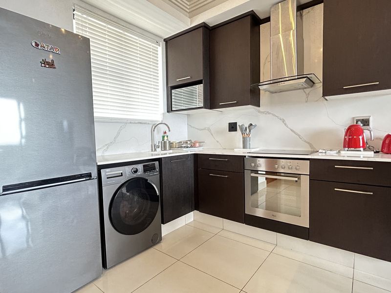 Modern kitchen featuring dark wood cabinetry, stone countertops, marble-look backsplash, and integrated stainless steel appliances, offering a sleek and functional cooking space.