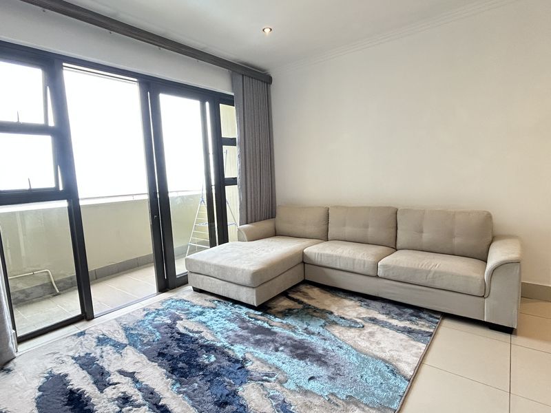 A bright living room featuring large sliding glass doors leading to a balcony, neutral tiled flooring, and recessed downlighting.
