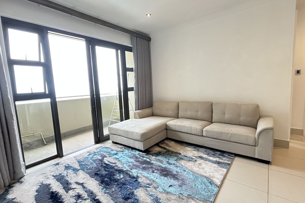 A bright living room featuring large sliding glass doors leading to a balcony, neutral tiled flooring, and recessed downlighting.