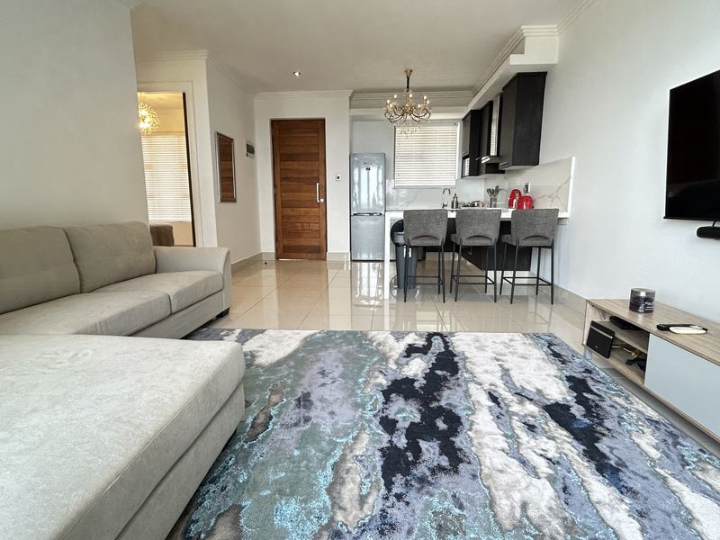 Modern open-plan living area featuring sleek tiled floors, a contemporary kitchen with breakfast bar, and high-quality finishes throughout this well-maintained apartment space.