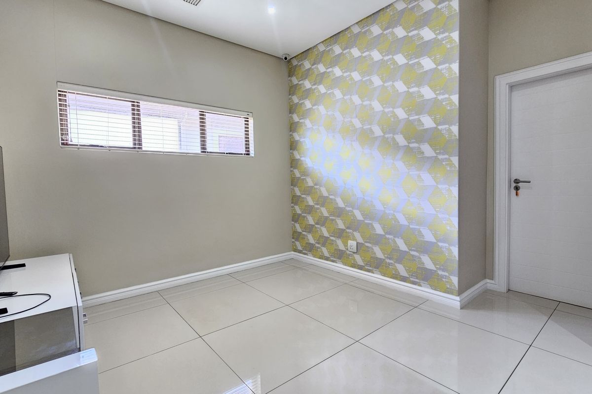 A bright bedroom featuring large format floor tiles, a decorative feature wall, and horizontal window blinds.