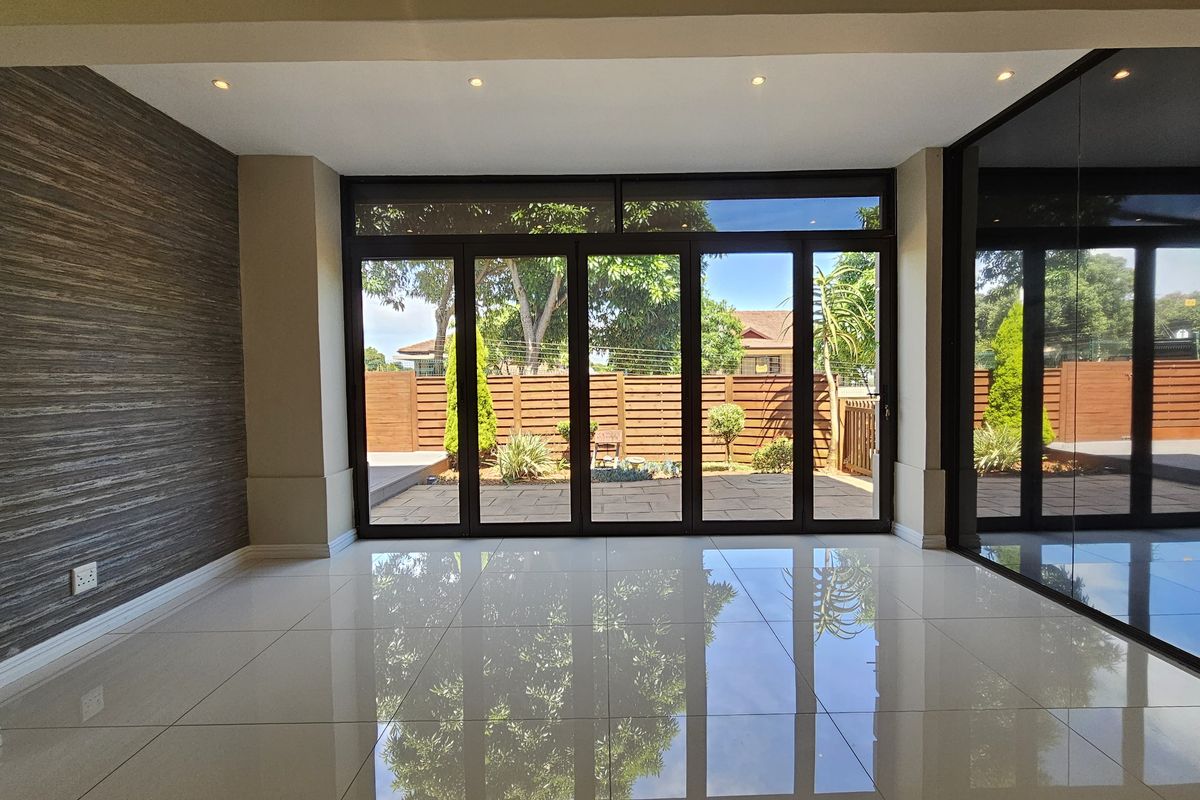 Spacious living area featuring large glass stacker doors that open onto a paved patio and garden, finished with polished porcelain floor tiles.