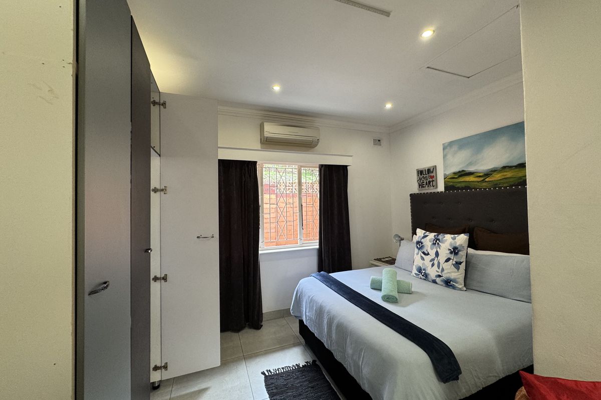 A well-lit bedroom featuring built-in cupboards, tiled flooring, and a wall-mounted air conditioning unit.