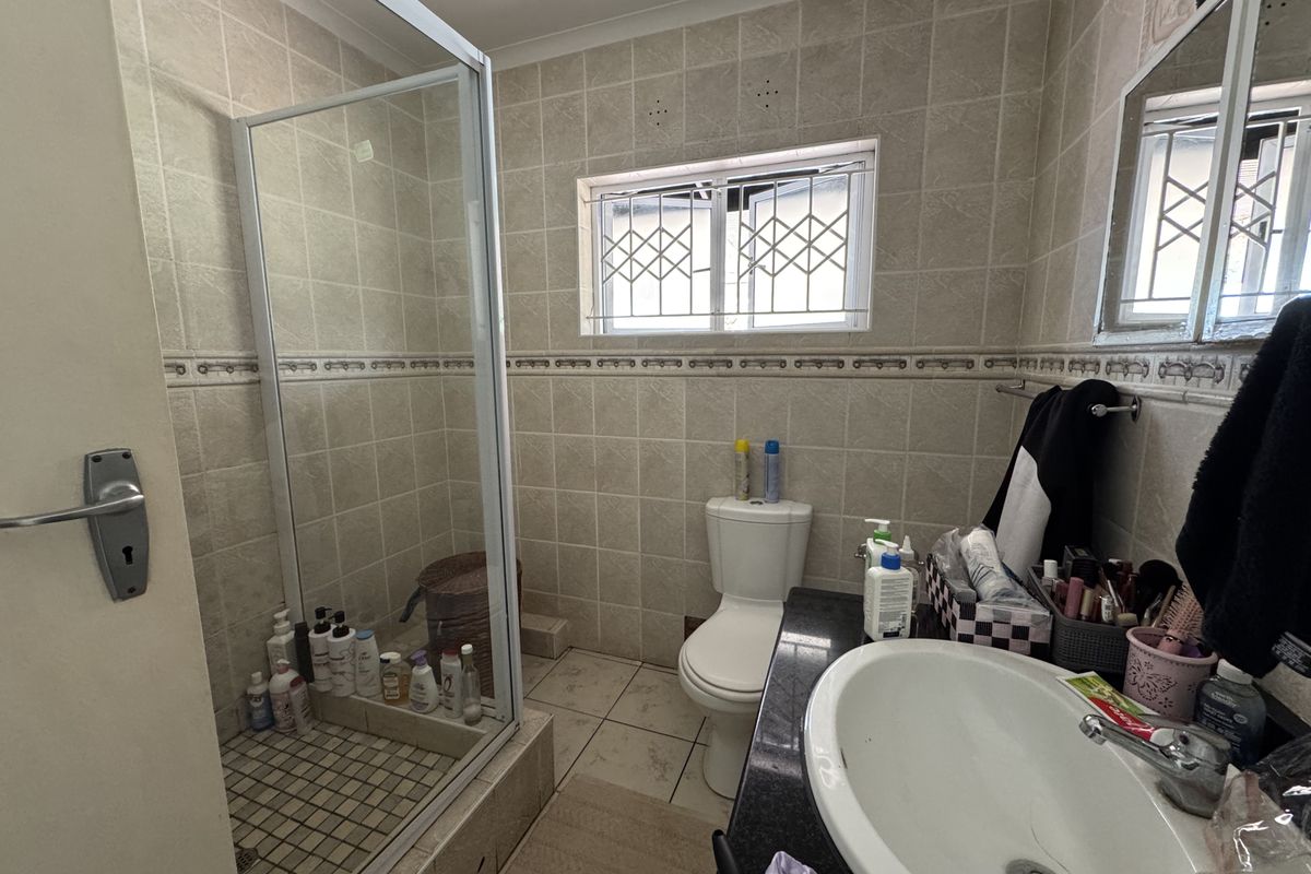 A functional bathroom featuring a glass-enclosed shower, a built-in vanity with a basin, and a toilet, finished with neutral wall and floor tiling.