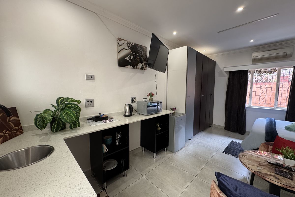 A compact open-plan living area featuring a kitchenette with stone-look countertops, built-in cabinetry, tiled flooring, and an integrated air conditioning unit.