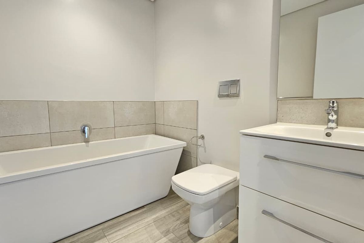 Modern bathroom featuring a sleek freestanding bathtub, wall-mounted toilet with concealed cistern, and a contemporary vanity unit with integrated basin.