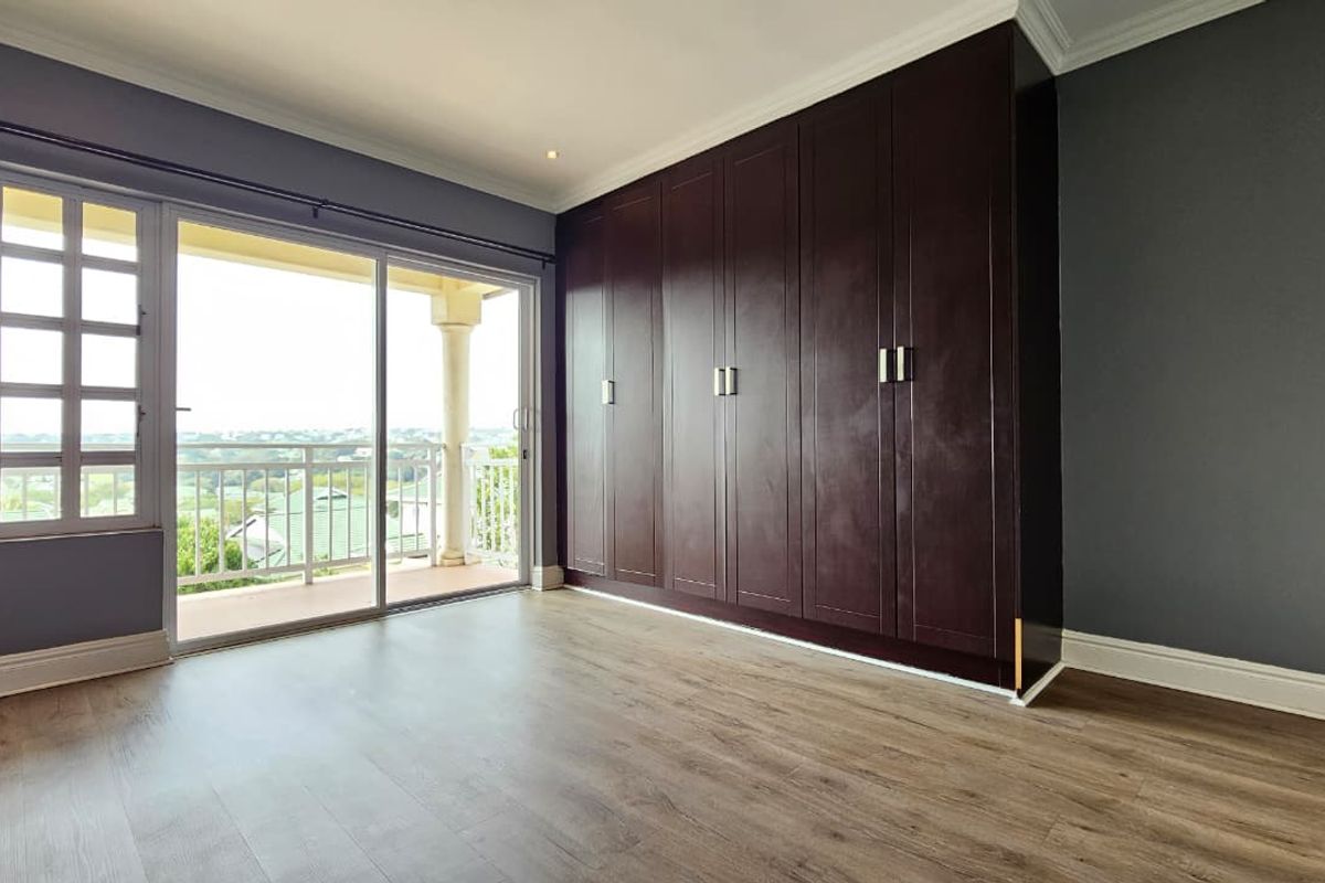 Spacious bedroom featuring dark wood built-in wardrobes, laminate flooring, and sliding glass doors opening onto a private balcony with scenic views.