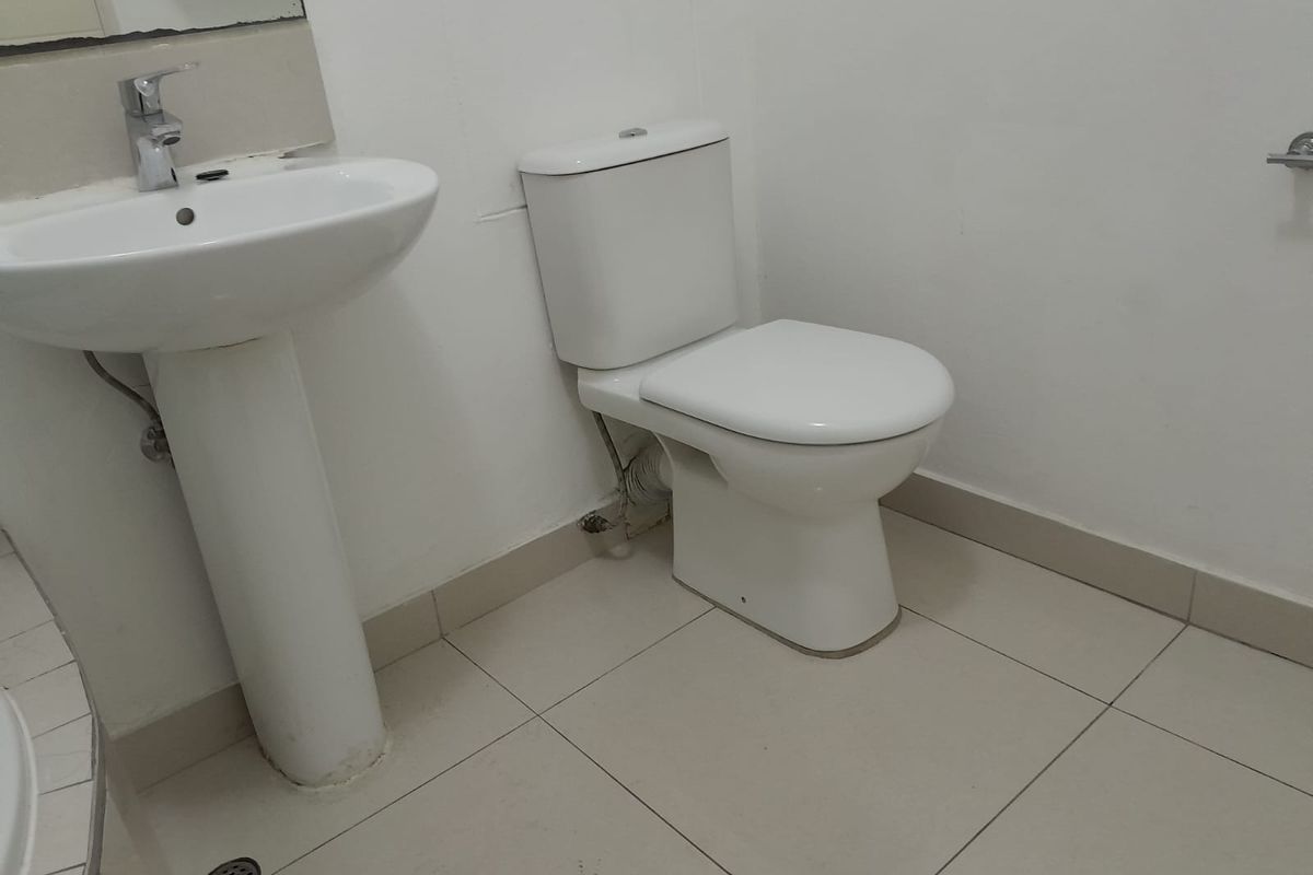 A functional bathroom featuring a white pedestal basin, a standard toilet, and tiled flooring.
