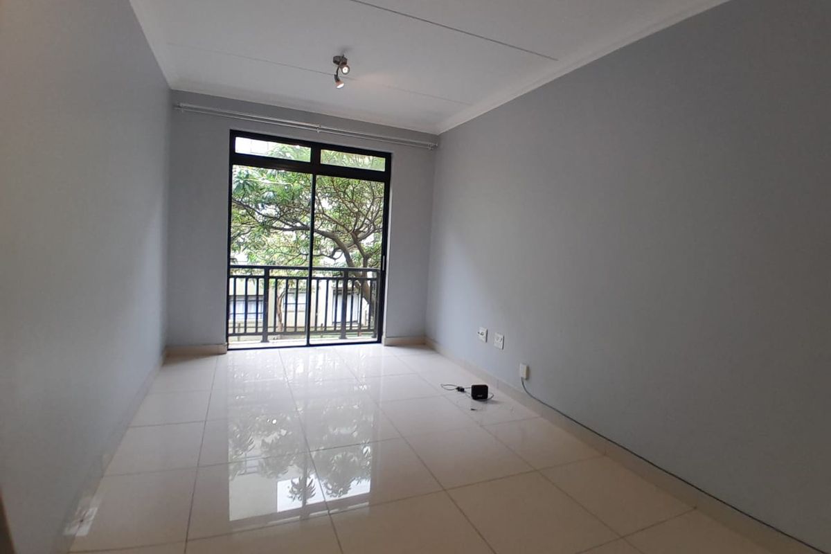 A bright, empty bedroom featuring neutral tiled flooring, light grey walls, and a sliding glass door leading to a balcony.
